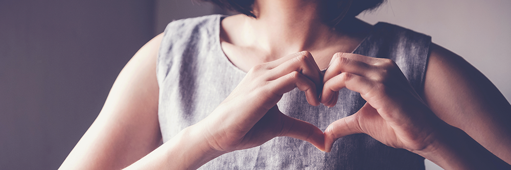 A woman with her hands forming a heart shape, signifying her dedication to volunteering.