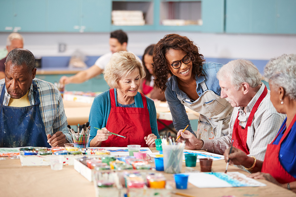 A group of enthusiastic retired seniors engrossed in an art class, guided by a teacher, at an Irish community center.