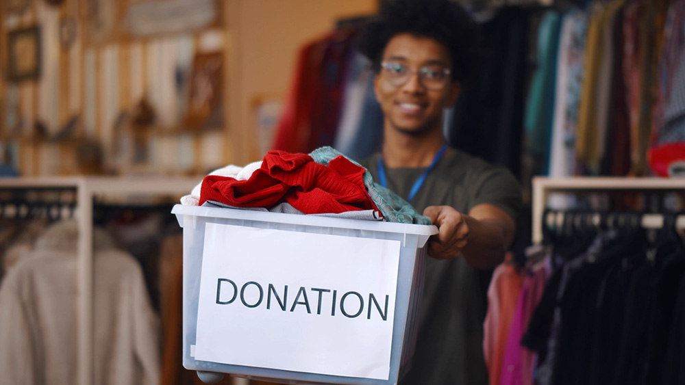 African American man holding a donation box and smiling at the camera in an Irish charity shop, 2023.